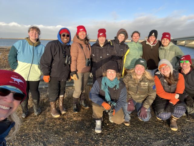 students standing on a river bank, in winter gear, smiling